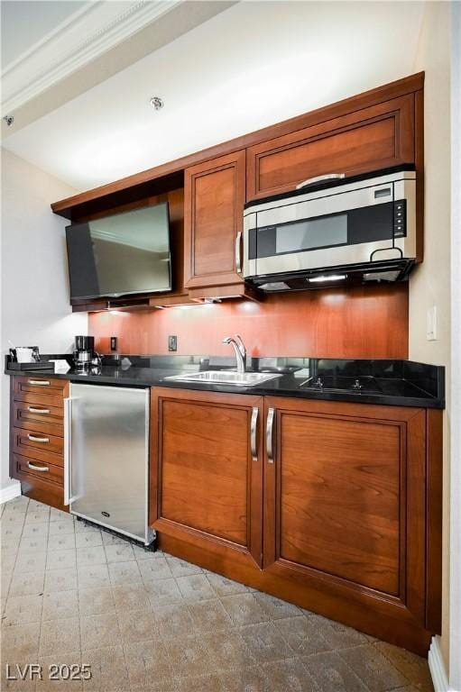 kitchen with a sink, appliances with stainless steel finishes, light floors, brown cabinetry, and dark countertops