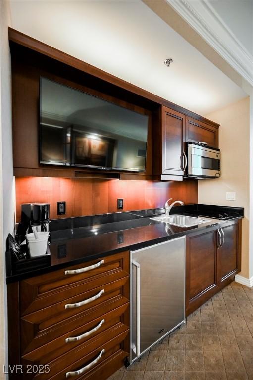 kitchen with stainless steel appliances, dark countertops, crown molding, and a sink