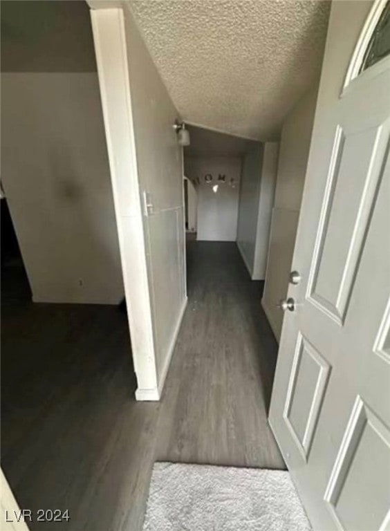 corridor with a textured ceiling, hardwood / wood-style floors, and vaulted ceiling