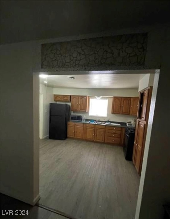 kitchen with light wood-type flooring, black refrigerator, and stove