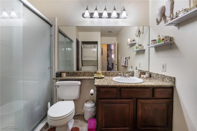 bathroom featuring a shower with shower door, vanity, stacked washer and clothes dryer, and toilet