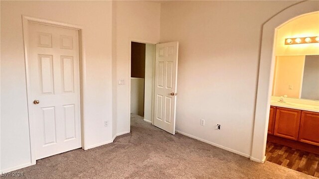 unfurnished bedroom featuring baseboards, ensuite bath, arched walkways, a sink, and dark carpet