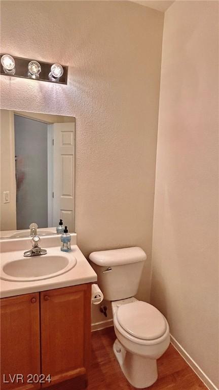 half bathroom with toilet, vanity, baseboards, and wood finished floors