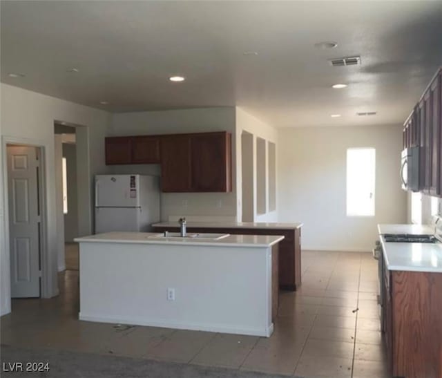 kitchen featuring stove, a kitchen island with sink, sink, and white fridge