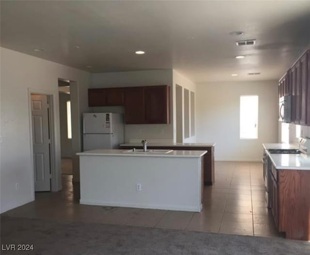 kitchen with light tile patterned floors, sink, stainless steel appliances, and an island with sink