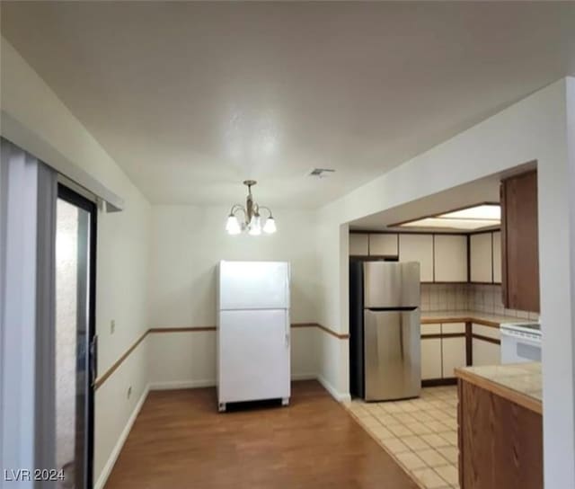 kitchen with stainless steel refrigerator, an inviting chandelier, white refrigerator, backsplash, and white cabinets