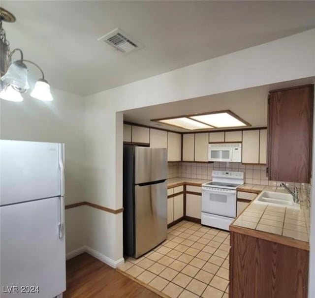 kitchen with sink, light hardwood / wood-style flooring, tile countertops, white appliances, and decorative backsplash