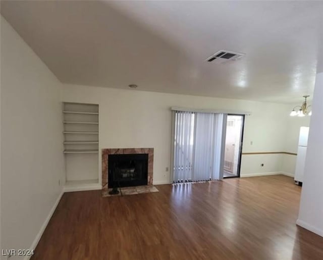 unfurnished living room with a chandelier, built in shelves, hardwood / wood-style flooring, and a tiled fireplace