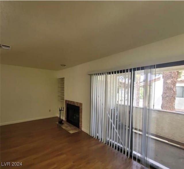 unfurnished living room with a fireplace, built in shelves, and dark hardwood / wood-style flooring