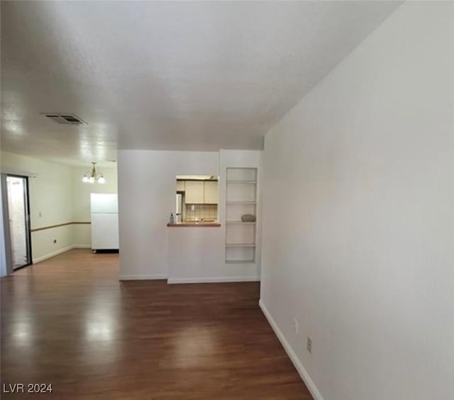 unfurnished living room featuring a notable chandelier, built in features, and dark wood-type flooring