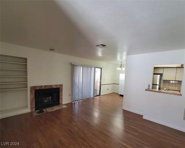 unfurnished living room featuring built in shelves, a tile fireplace, a notable chandelier, and hardwood / wood-style flooring