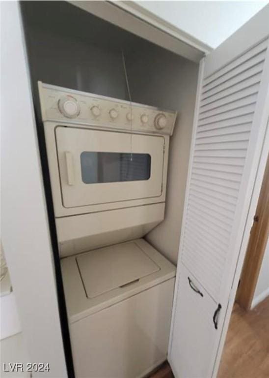 washroom with stacked washing maching and dryer and light hardwood / wood-style flooring