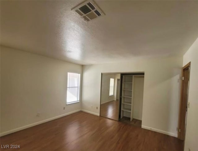 unfurnished bedroom with a textured ceiling, a closet, and dark wood-type flooring