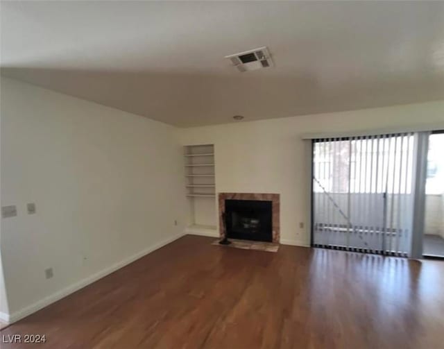 unfurnished living room with built in shelves, a fireplace, and dark wood-type flooring