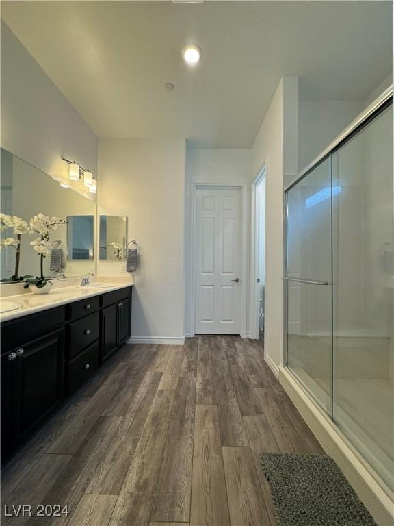 full bathroom featuring a sink, wood finished floors, baseboards, double vanity, and a stall shower