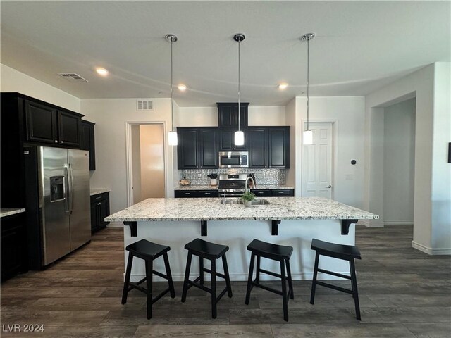 kitchen with tasteful backsplash, dark hardwood / wood-style flooring, appliances with stainless steel finishes, a kitchen island with sink, and sink