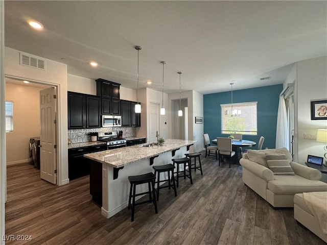 kitchen featuring visible vents, dark cabinets, a kitchen island with sink, stainless steel appliances, and pendant lighting