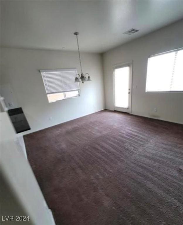 unfurnished living room with a notable chandelier and dark carpet