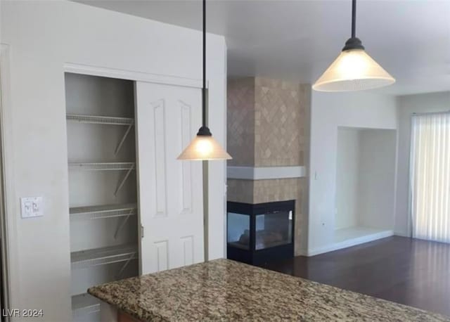 kitchen with a tiled fireplace, hanging light fixtures, stone countertops, and dark hardwood / wood-style flooring