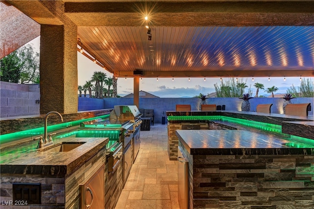 patio terrace at dusk featuring sink, a grill, a fenced in pool, and exterior kitchen