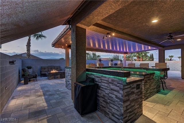 patio terrace at dusk featuring an outdoor bar, a gazebo, ceiling fan, and a fire pit