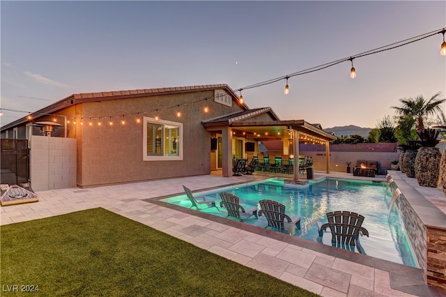 pool at dusk featuring a lawn, a patio, and pool water feature