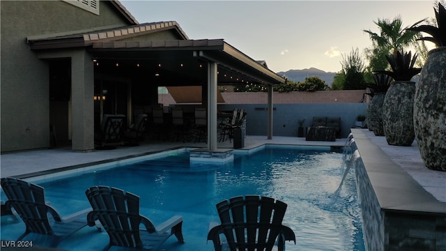 pool at dusk with a pergola, a patio area, and pool water feature