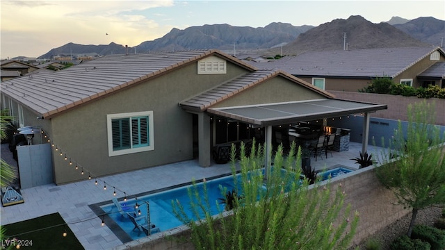 back house at dusk with a patio, a mountain view, and a fenced in pool