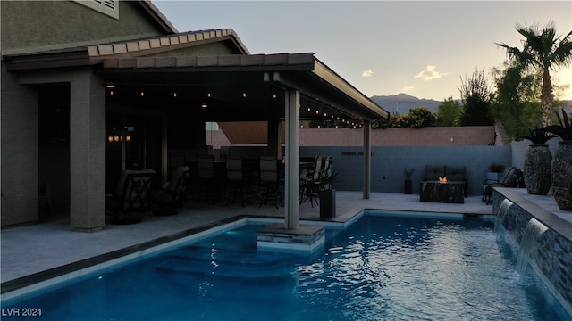 pool at dusk with a patio and pool water feature