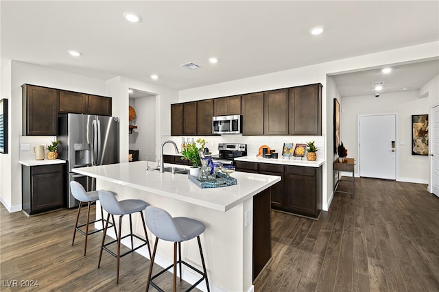 kitchen featuring a breakfast bar, stainless steel appliances, an island with sink, sink, and dark wood-type flooring