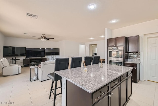 kitchen with a kitchen island, backsplash, a kitchen breakfast bar, dark brown cabinetry, and stainless steel double oven