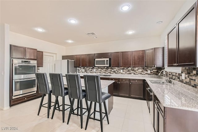 kitchen featuring sink, a breakfast bar, appliances with stainless steel finishes, a center island, and tasteful backsplash