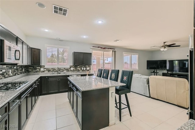 kitchen with a kitchen bar, sink, light stone counters, a kitchen island, and stainless steel appliances