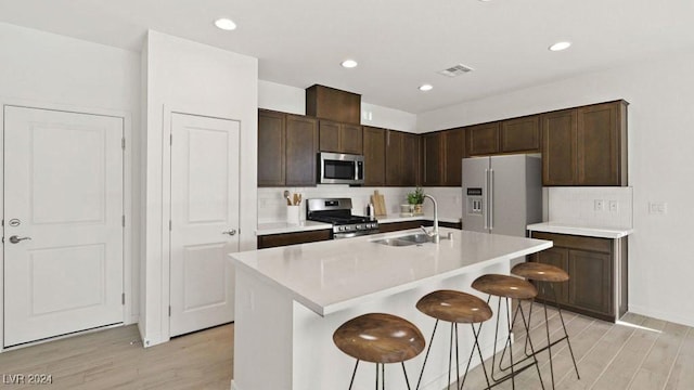 kitchen with light wood finished floors, a breakfast bar area, appliances with stainless steel finishes, and a sink