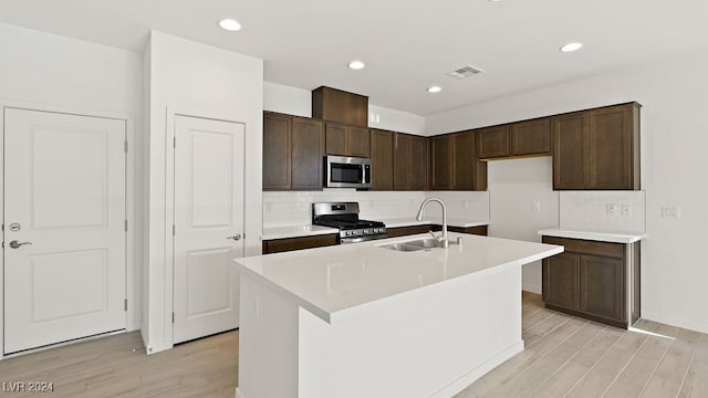 kitchen with appliances with stainless steel finishes, a sink, dark brown cabinets, light wood-style floors, and backsplash