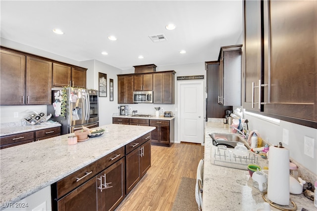 kitchen with light hardwood / wood-style flooring, light stone counters, dark brown cabinets, stainless steel appliances, and sink