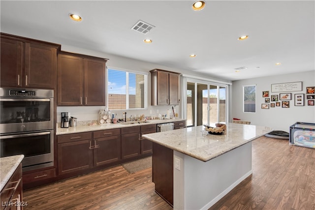 kitchen featuring stainless steel double oven, dark hardwood / wood-style floors, a healthy amount of sunlight, a kitchen island, and sink