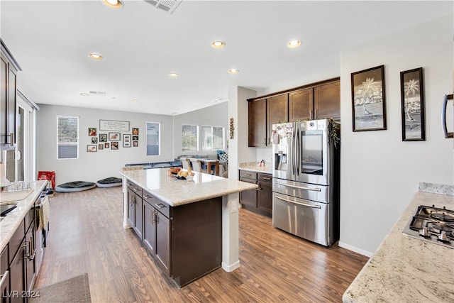 kitchen featuring stainless steel appliances, hardwood / wood-style floors, a kitchen island, dark brown cabinetry, and light stone counters