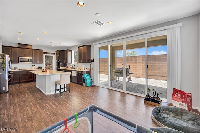 interior space featuring appliances with stainless steel finishes, dark wood-type flooring, a kitchen island, and dark brown cabinetry