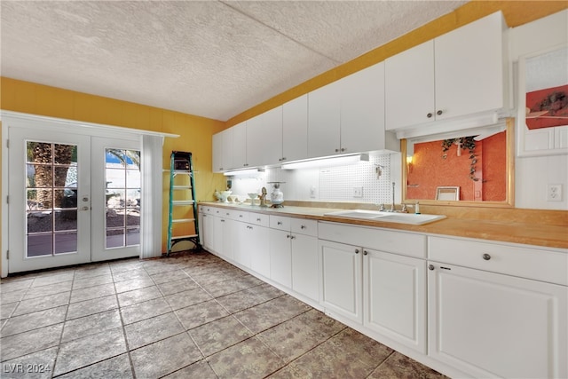 kitchen with a textured ceiling, french doors, sink, and white cabinetry