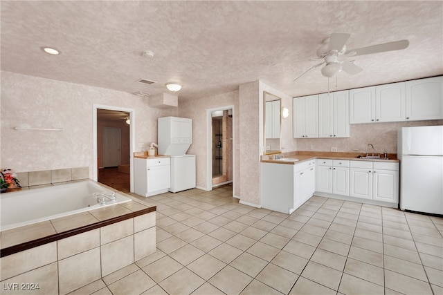 kitchen featuring ceiling fan, stacked washer / dryer, white fridge, and white cabinetry