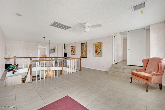 living area with ceiling fan, a textured ceiling, and light tile patterned floors