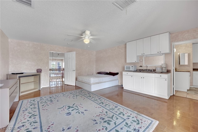 kitchen featuring a textured ceiling, parquet flooring, white cabinets, ceiling fan, and sink