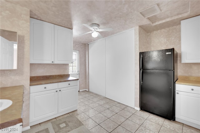 kitchen with white cabinets, light tile patterned flooring, black refrigerator, and ceiling fan