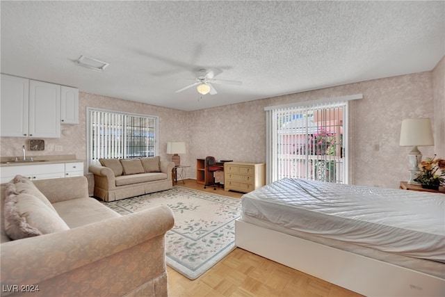 bedroom featuring ceiling fan, sink, a textured ceiling, and light parquet floors