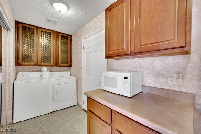 laundry room with washing machine and clothes dryer, a textured ceiling, cabinets, and light tile patterned floors