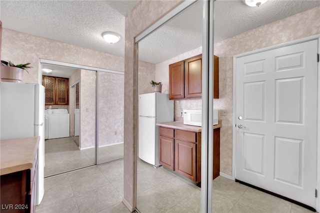 bathroom with a textured ceiling, washing machine and clothes dryer, and tile patterned flooring