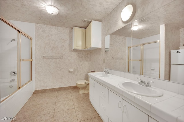 full bathroom featuring a textured ceiling, toilet, tile patterned floors, enclosed tub / shower combo, and dual vanity