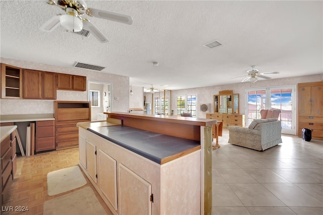 kitchen featuring ceiling fan, a kitchen island with sink, a textured ceiling, and light parquet flooring