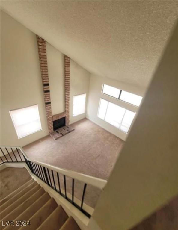 staircase with a fireplace, a textured ceiling, brick wall, and carpet floors